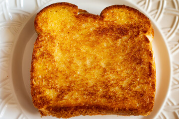 A hot grilled cheese on a white plate made at home with basic loaf bread and cojack cheese.
