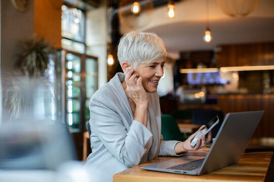 Senior businesswoman working on laptop in a cafe with wireless earbuds