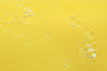 Essential oil bubbles on yellow background, macro view. Cosmetic product