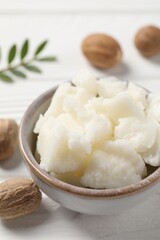 Shea butter in bowl and nuts on white wooden table, closeup