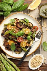 Delicious salad with grilled vegetables, basil, pesto sauce, pine nuts and fork on wooden table, flat lay