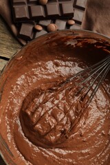 Chocolate dough in bowl and whisk on wooden table, top view