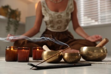 Young woman practicing yoga on floor indoors, focus on smoldering incense stick and tibetan singing...