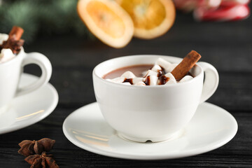 Tasty hot cocoa drink with marshmallows in cups and spices on black wooden table, closeup