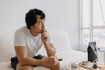 Vacant absent minded Asian man staring out the windows, holding a coffee cup.