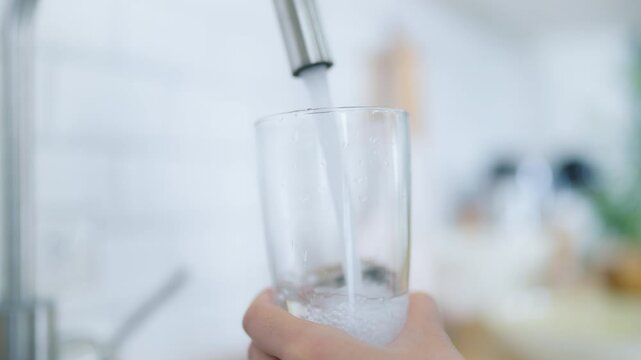 Hand of Asian woman pouring clean tap drinking water into the clean glass in kitchen room