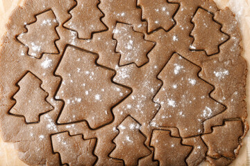 Cooking ginger cookies, Christmas and New Year traditional cookies in shape of Christmas fir tree, raw rolled out dough with cut out dough figures, close up texture, top view, pattern on dough