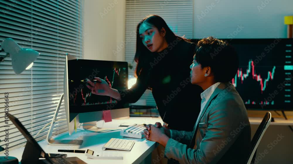 Poster businesswoman points at data on a computer monitor while talking to a colleague in their office. the