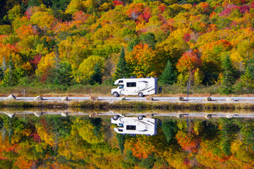 RV traveling on a NH road during fall foliage with reflection in lake