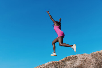 Woman jumping joyfully on a rock under a clear blue sky