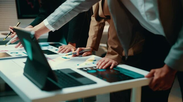 Businesspeople in a meeting room are pointing at documents and using interactive touchscreen to analyze financial data displayed on it