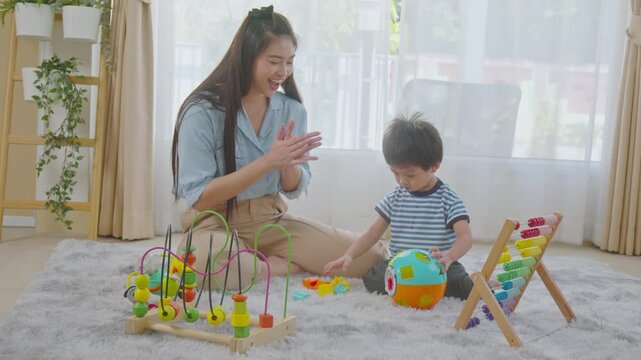 Heartwarming Asian mother engaging with her young son as they play with educational toys on a soft, cozy rug. Mother smiling warmly while the child is focused on the colorful abacus and bead maze