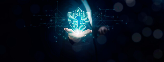 Businessman using mobile phone and showing shield icon on palm against dark background with empty space for text. Cyber security information concept.