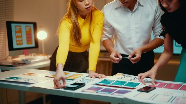 Three asian ui/ux designers are working together on a new mobile application. They are using paper prototypes to test different design ideas