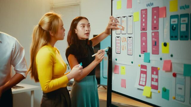 Two women, possibly web designers or developers, are having a discussion about ux ui design. They are both looking at a whiteboard with wireframes and notes on it