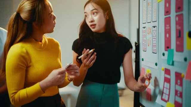 Team of asian web designers collaborating on a user interface design project for a mobile application, discussing ideas and strategies in a creative office environment