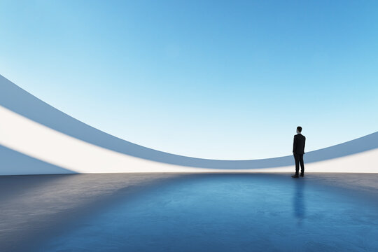 Businessman standing in a futuristic, minimalistic architectural space with blue sky and curved white walls.