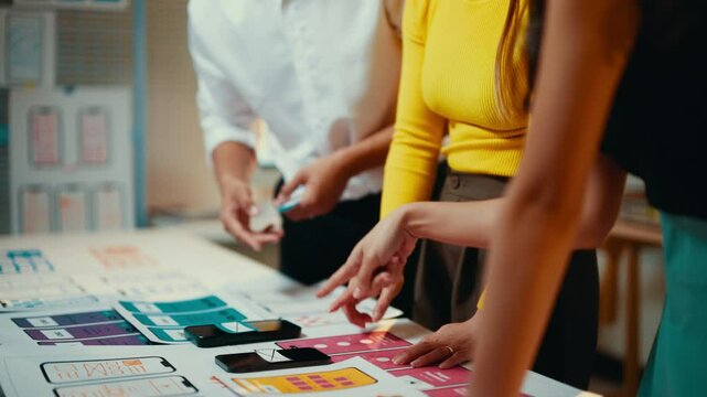 Ui designers collaborate at an office desk, reviewing wireframe sketches for a mobile application. The team focuses on enhancing user experience through creative brainstorming and planning