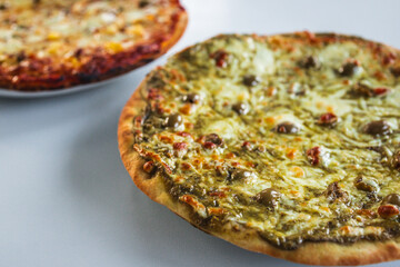 pesto pizza with olives next to pineapple pizza