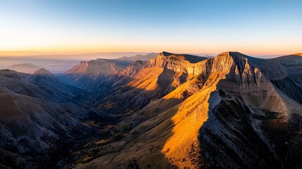 Naklejka premium A mountain landscape at golden hour, with the peaks bathed in golden light, creating long shadows across the valley below