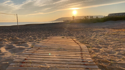 A path of small wooden planks leads to the sea on the right and from the beach volleyball court....