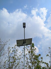 Solar-powered street light against a blue sky with white clouds. Sustainable lighting solution for outdoor spaces.
