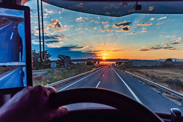 View from the driver's seat of a truck on a highway at dawn with the sun on the horizon and a...
