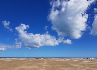 View of the beach and blue sky with white cumulus clouds.