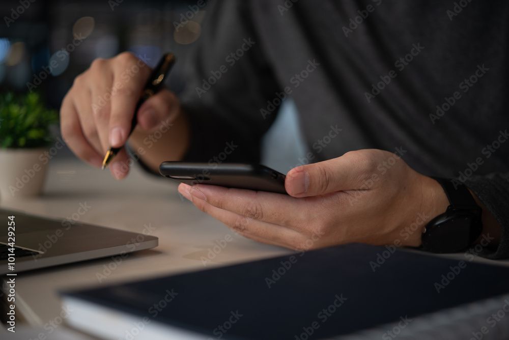Poster businessman using a smartphone while holding a pen, multitasking between mobile communication and pl
