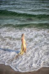 Beautiful blonde model walks along the seashore in a yellow dress in a storm.