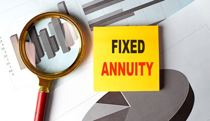 Sticky note with the text fixed annuity , placed on financial charts with a magnifying glass and red handle