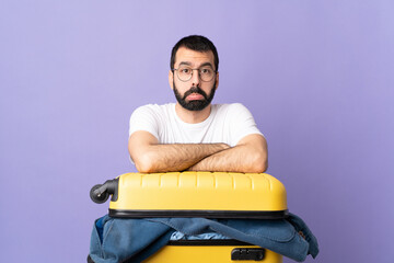 Traveler caucasian man with a suitcase full of clothes over isolated purple background with sad...