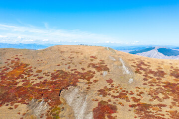 Hikers one behind the other in a hiking line on the ridge of a beautiful mountain during autumn with colorful vegetation - drone aerial shot