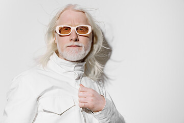 Fashionable elderly man with long white hair and glasses in a stylish white outfit against a plain...