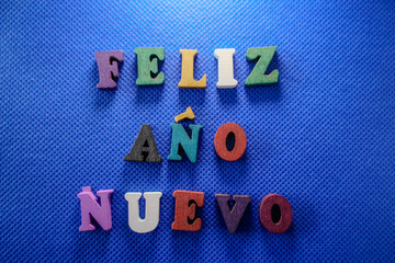 New Year's greetings 2025, in Spanish, with colorful and wooden letters, on a blue background © santirj 
