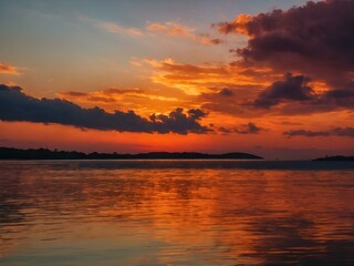 Obraz premium The sky at sunset, with vivid orange and red tones reflecting on the water and distant clouds catching the last rays of the sun 