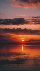 Obraz premium The sky at sunset, with vivid orange and red tones reflecting on the water and distant clouds catching the last rays of the sun 