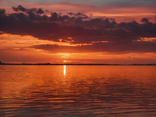 Fototapeta premium The sky at sunset, with vivid orange and red tones reflecting on the water and distant clouds catching the last rays of the sun 