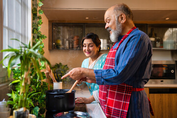 Senior Indian couple bonding over cooking, enjoying retirement life in their modern kitchen