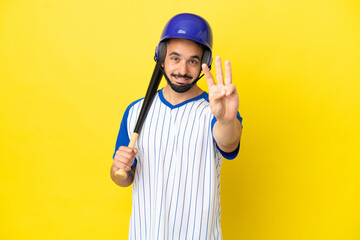 Young caucasian man playing baseball isolated on yellow background happy and counting three with fingers