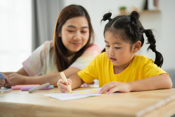 A young girl is drawing with a marker on a piece of paper while her mother watches. Concept of bonding and learning