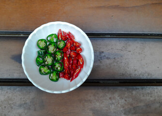 Slice of Green and red chili pepper on a plate. Wood background