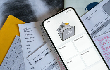 Ein Smartphone auf dem gerade eine elektronische Patientenakte angezeigt wird, liegt auf...