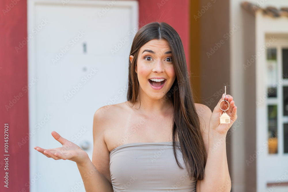 Wall mural girl holding home keys at outdoors with shocked facial expression