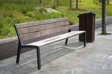 wooden and metal bench alongside a matching trash bin on the sidewalk, symbolizing urban design and...