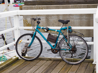 Blue Bicycle on Wooden Pier by Water with White Railing and Blurred Background
