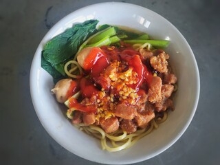 Mie Ayam or noodles chicken is an Indonesian dish made from yellow wheat noodles seasoned with chicken and vegetables. isolated on grey table, top view