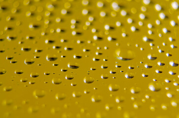 Side view of raindrops forming patterns on a smooth surface on yellow background. Fresh rain texture