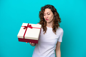 Young caucasian woman holding a gift isolated on blue background with sad expression