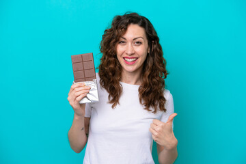 Young caucasian woman isolated on blue background taking a chocolate tablet and with thumb up